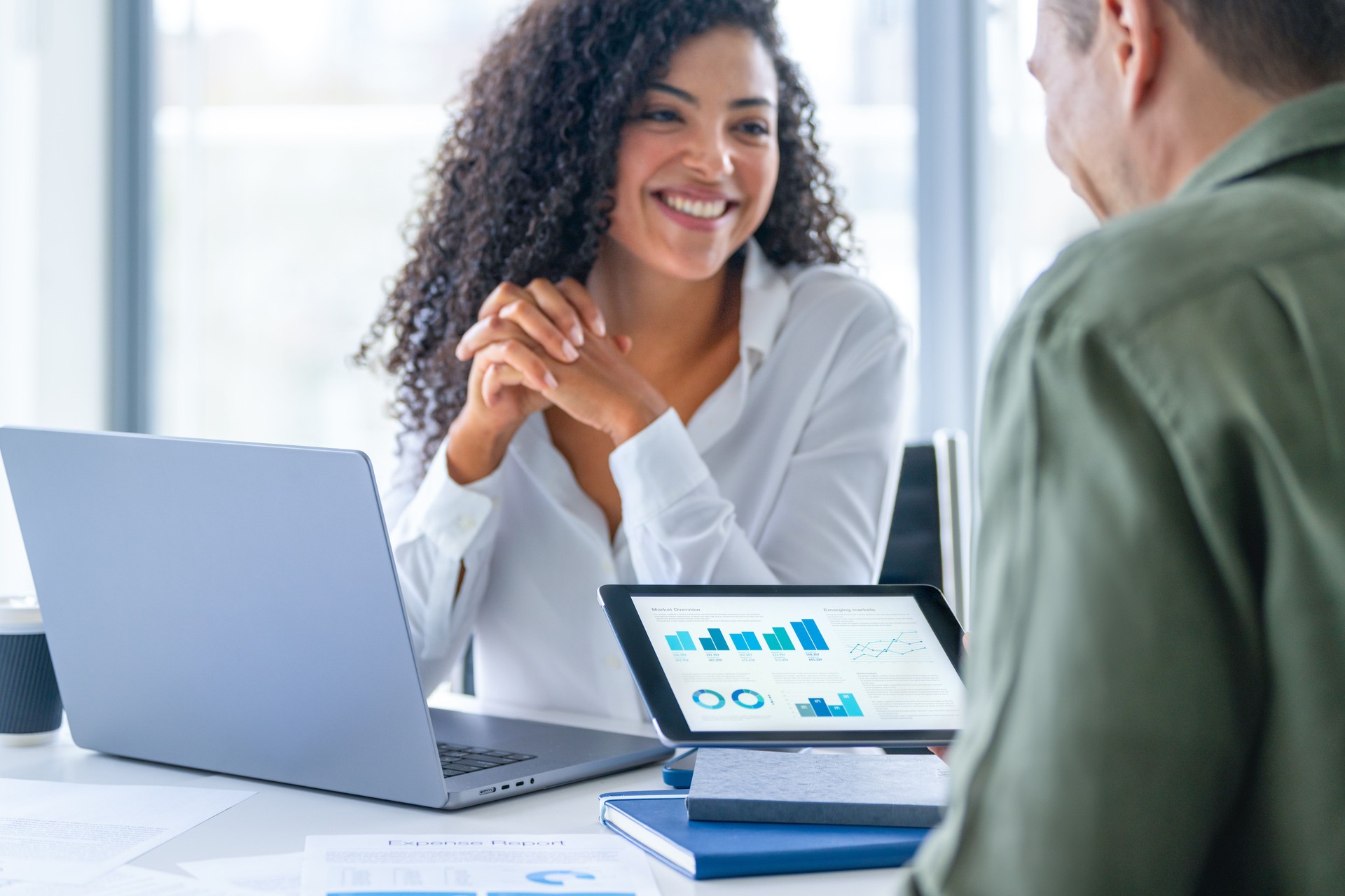 Business man and business woman in a meeting at the office. There is a laptop on the table and the man is holding a digital tablet with finance chart and graphs